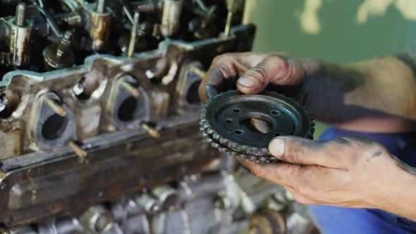 An Auto Mechanic Holds a Gearwheel in His Hands
