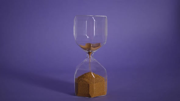 Glass Hourglass with Golden Sand on Purple Background