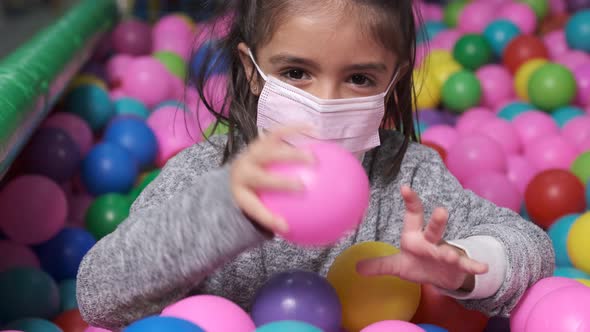 Happy 5 year old girl with mask in a ball pool throwing balls to camera