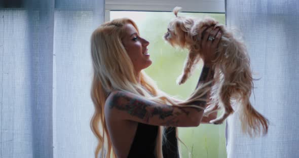 Beautiful young blonde woman holding and kissing her yorkshire terrier dog