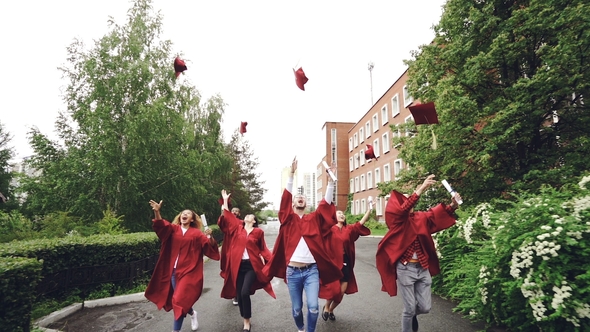 of Cheerful Friends Students Running on Campus with Diplomas, Throwing Mortarboard Caps, Catching