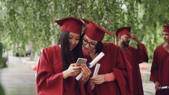 Female Graduates Are Using Smartphone Standing Outdoors
