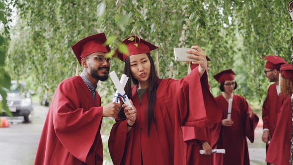 Fellow Students Are Taking Selfie with Diplomas Posing and Smiling, Girl Is Holding Smartphone