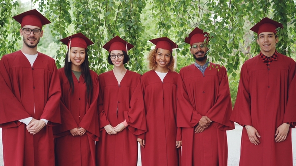 Portrait of Multiethnic Group of Graduating Students Standing Outdoors Wearing Red Gowns and Mortar