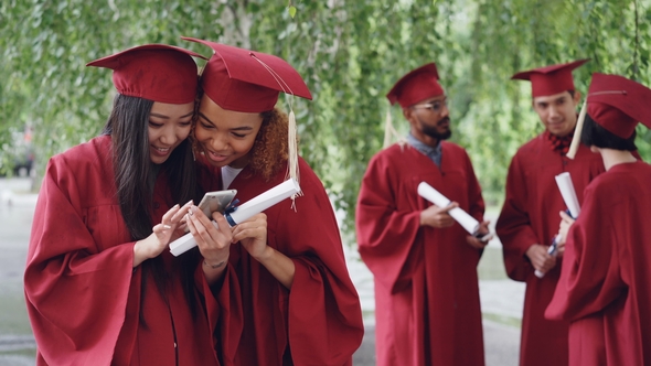 Attractive Young Women Happy Graduates Are Watching Photos on Smart Phone and Talking on Graduation