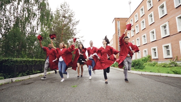 Dolly Shot of Joyful Graduating Students Running with Diplomas Waving Mortar-boards and Laughing