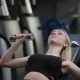 Cute Blonde Girl with Straight Hair in a Black Sport Wear with Blue Eyes Does a Dumbbell Press on an - VideoHive Item for Sale