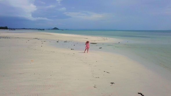 Aerial View of Young Carefree Woman in Pink Sundress Walking Along Remote White Sandy Beach