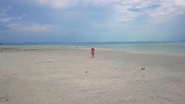 Aerial View of Young Carefree Woman in Pink Sundress Walking Along Remote White Sandy Beach with