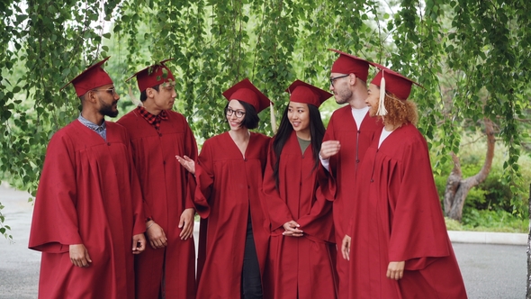 Portrait of Excited Graduating Students Multiethnic Group Standing Outdoors in Red Gowns and Mortar