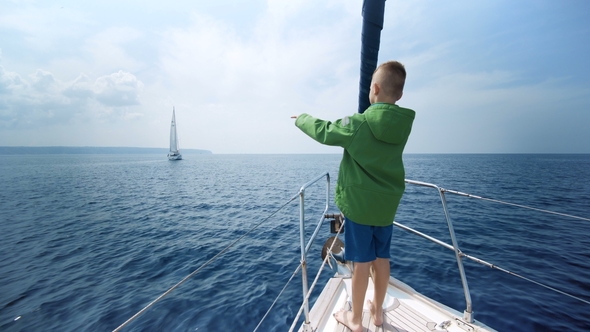 Little Boy Stands on the Bow of the Yacht and Shows the Way