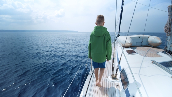 Little Boy Stands on the Bow of the Yacht and Shows the Way