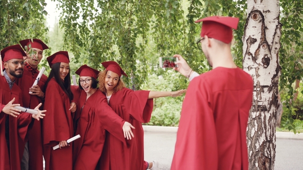 Graduating Student Is Recording Video of His Friends in Gowns Holding Diplomas, Waving Hands and