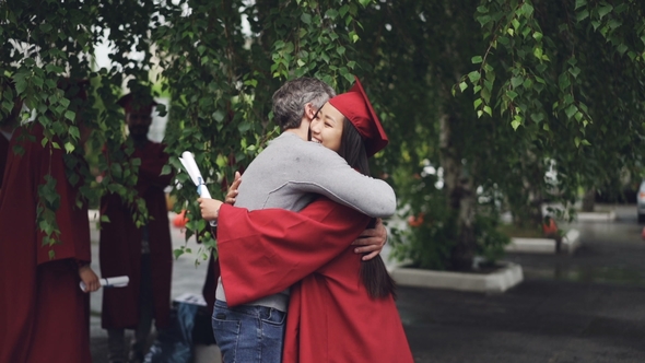 Loving Father Is Congratulating His Daughter on Graduation Day, People Are Hugging and Laughing