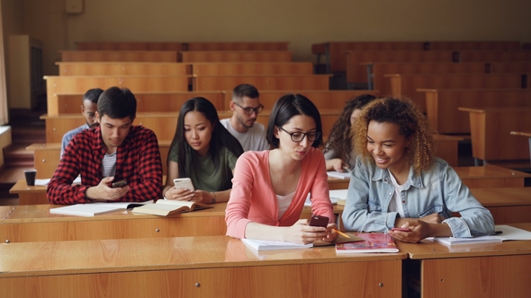 Young People Are Using Smartphones and Talking Sitting at Desks in Lecture Hall at University