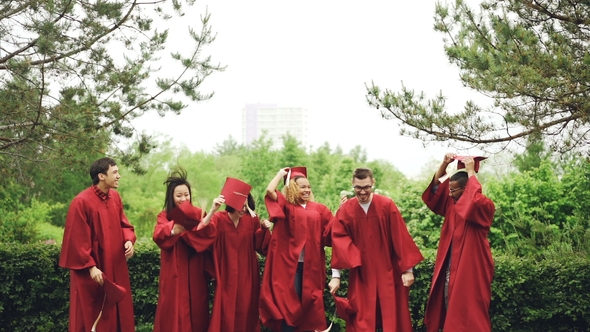 of Joyful Students Throwing Mortarboards in Air and Catching Them, Laughing and Enjoying Graduation