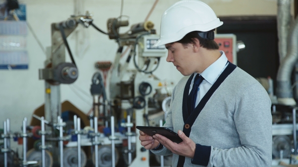 Young Engineer in Helmet Works with Table on the Factory