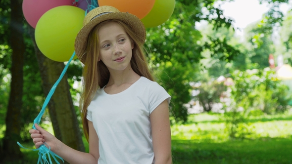 Portrait of Pretty Girl Poses at Camera with Colourful Balloons in Sunny Park