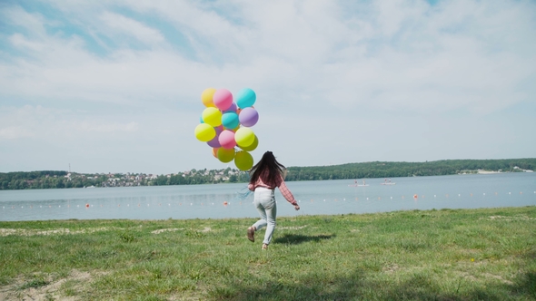 Happy Young Girl Running with Colourful Balloons To the Lake the Lake