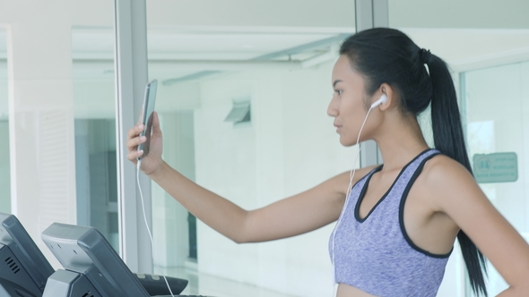 Asian Girl Running on Treadmill and Talking on the Phone