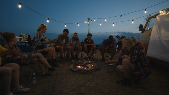 Friends Frying Sausages on Campfire in Twilight