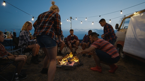 Friends Frying Sausages on Campfire in Twilight