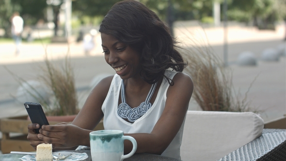 African American Woman Using Phone, While Sitting in Outside Cafe