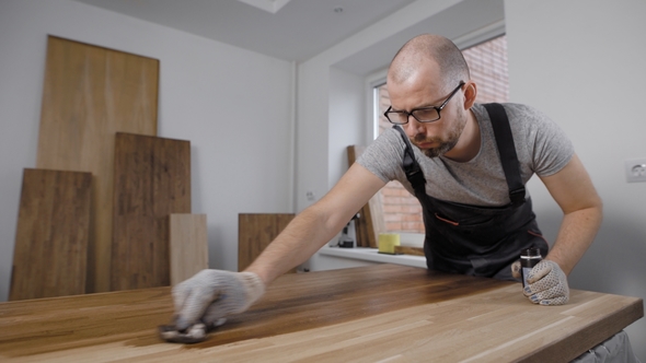 Worker in Overall and Gloves Putting Polish on Wooden Panel Indoors alt