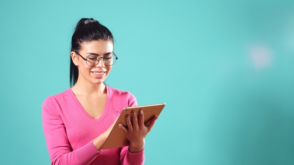 Young Cheerful Girl with Black Hair, Poses on a Blue Background with Tablet in Hands.