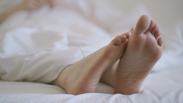 Delicate Female Feet Moving Toes Playfully on White Bedding