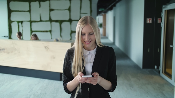 Young Formal Woman Using Smartphone in Office. Stylish Blond Woman in Jacket 