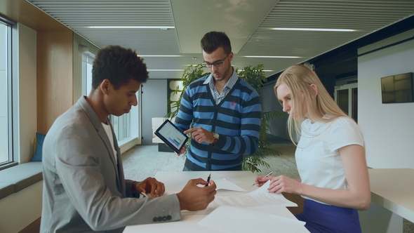 Multiethnic Coworkers with Papers and Tablet. Side View of Black Man with Coworkers at Table Reading