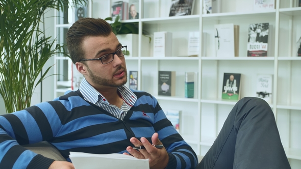 Man with Papers Talking in Office. Adult Stylish Man in Glasses Sitting on Sofa with Papers and