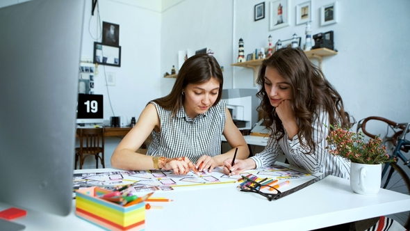 Young Female Architects Discussing with Blueprint in Office