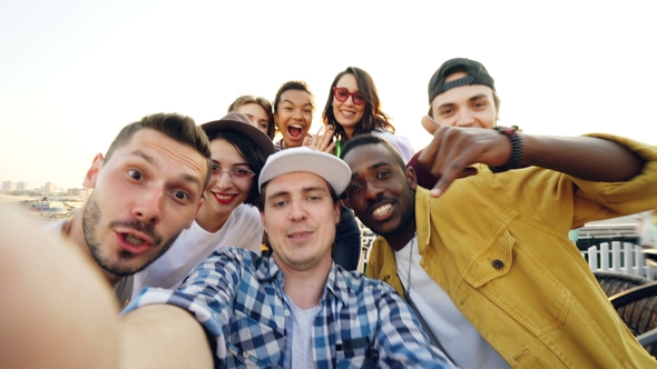 Handsome Young Man in Cap Is Looking at Camera Then Calling His Friends To Take Selfie, People Are