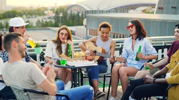 Attractive African American Girl Is Playing the Guitar, Her Friends Are Singing, Drinking