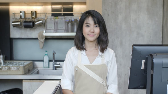 Portrait of Asian Female Barista Crossing Hands and Smiling on the Camera in the Coffee Cafe.