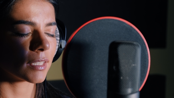 Young Beautiful Brunette Woman Recording Voice, Song or Album in Professional Studio. Girl Sings
