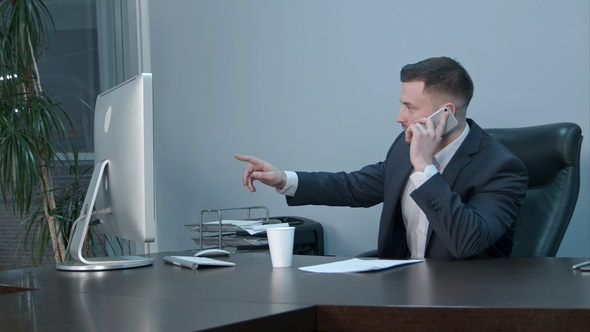 Young Caucasian Businessman Calling with Smartphone and Talking Seriously in Office