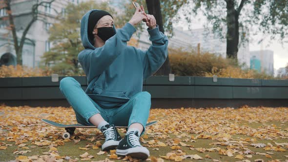 Young Hipster Woman with Face Mask Taking Selfies in the Park While Sitting on the Skateboard Alone