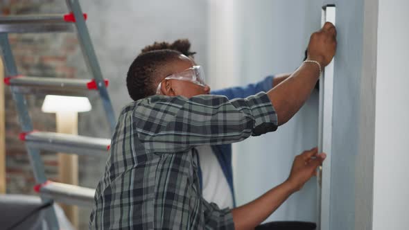 Black Guys Check Wall with Spirit Level Working in Apartment