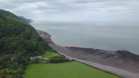 Rotating wide aerial looking west along the forest-like coast of Exmoor. Large sea, and amazing clif