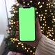 Woman holding modern smartphone with green screen chromakey near Christmas tree lights on background - VideoHive Item for Sale
