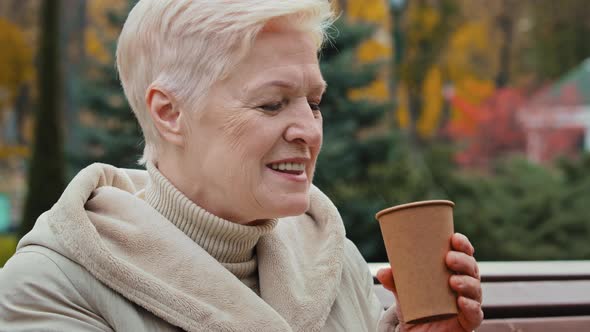 Carefree Dreamy Elderly Mature Woman Grandma Resting in Park Drink Hot Aromatic Coffee From