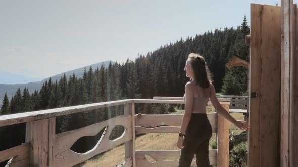 Woman comes out of a wooden hut with mountain view in the morning