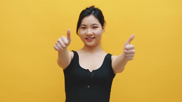 Beautiful Young Asian Woman with Thumbs Up Isolated on Yellow Background