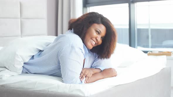 Beautiful Awesome Woman Has Joyful Expression, Lies on Stomach in Bed