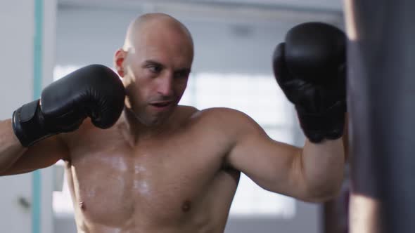 Caucasian male trainer wearing boxing gloves training with punching bag at the gym