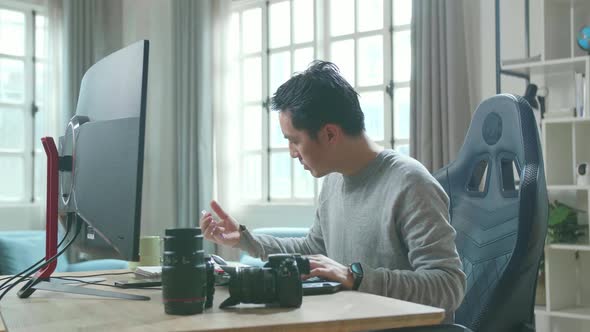 Asian Cameraman Looking At Computer And Writing In Notebook On A Table While Working At Home