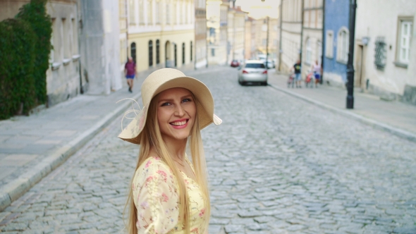 Smiling Woman Walking on Street. Cheerful Pretty Woman in White Hat Looking Back at Camera 